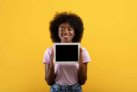 African american lady demonstrating digital tablet with free screen, mockup for text or advertisement, yellow backgroundの写真素材
