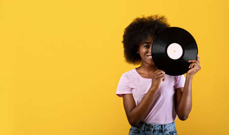Retro music concept. Excited african american lady holding vinyl record and smiling on yellow background, panoramaの写真素材