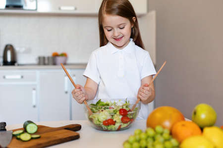 Happy Little Girl Cooking Dinner Making Fresh Salad In Kitchenの写真素材