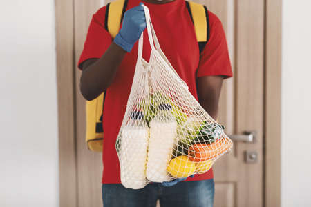 Black delivery man holding net mesh bag with groceriesの写真素材