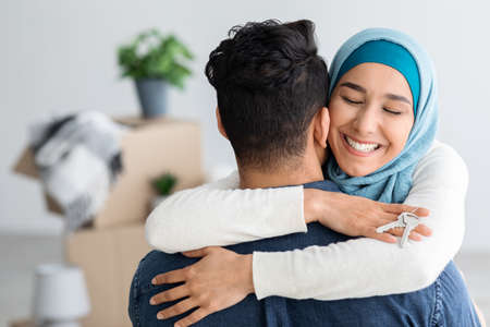 Happy lady in hijab with keychain hugging her husbandの写真素材