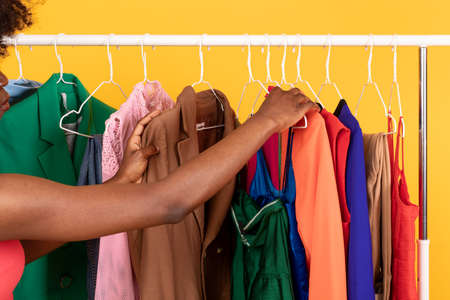 Black Woman Choosing Clothes On Rail Over Yellow Background, Cropped