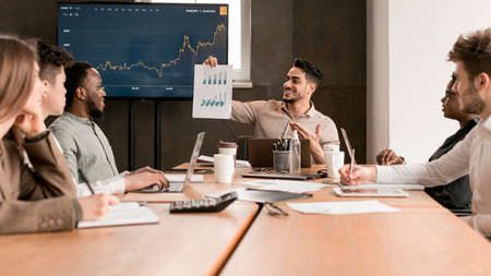 Employee showing paper with graph diagram, sitting at deskの写真素材