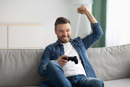 Emotional middle-aged man playing video games at homeの写真素材