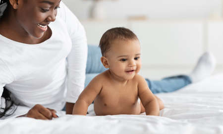 Cute little African American baby crawling in bed with mom