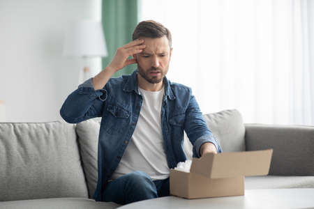 Disappointed man customer checking mail box at homeの写真素材