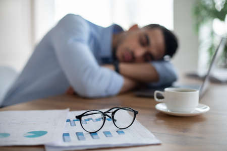Exhausted Arab businessman sleeping on his office desk, tired of overworking, selective focus on documents and glassesの写真素材