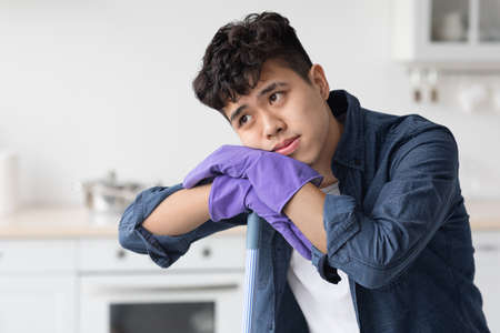 Tired asian guy leaning on broom, looking at copy spaceの写真素材