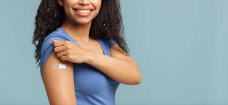 Successful covid-19 vaccination. Happy unrecognizable black woman showing arm with plaster, blue background, free spaceの写真素材