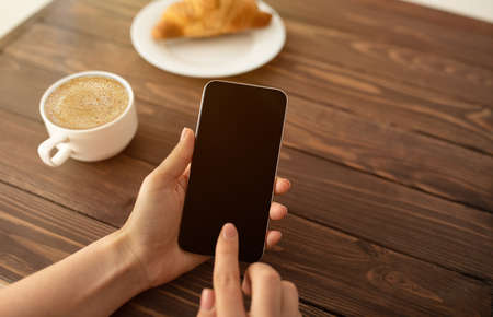 Cool app. Woman using smartphone with black screen and drinking coffee at cafe, closeup