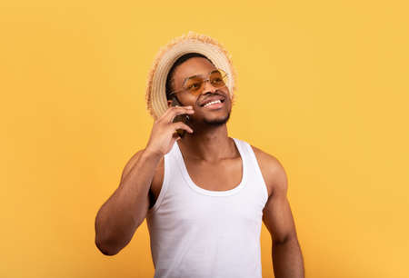 Positive black man in summer wear calling on smartphone, having pleasant conversation over yellow studio backgroundの写真素材