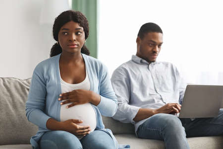 Lonely pregnant african woman sitting by her husband using laptopの写真素材