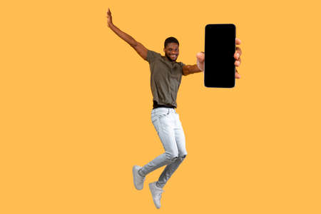 Cool mobile app. Excited black guy showing smartphone with blank black and jumping over yellow...