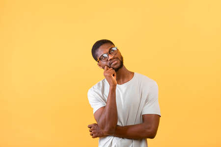Searching for idea. Thoughtful african american guy looking up at free space, posing over yellow...