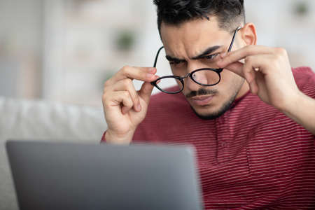 Arab guy with glasses using laptop, having vision problems