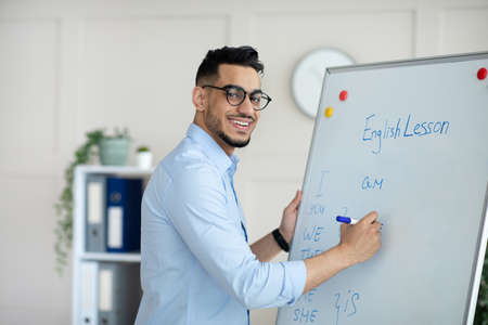 Young Arab male teacher giving online class, explaining new material, writing English rules on blackboard at home officeの写真素材