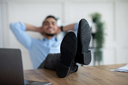 Young Arab employee relaxing after successful work, putting legs on table at office, selective focusの写真素材