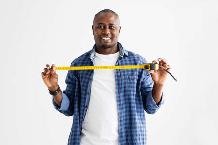 Home repairman. Happy african american man holding measuring tape and smiling at camera over white backgroundの写真素材