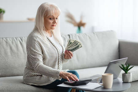 Mature woman using calculator and holding money