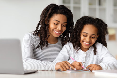 Happy black mother helping daughter with homeworkの写真素材