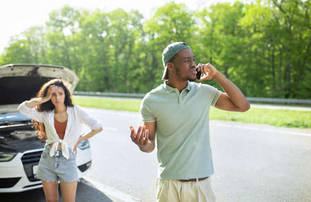 Young man calling for help with broken car, speaking to rodside assistance service, his upset...