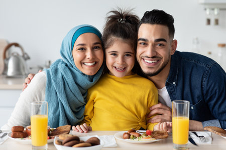 Happy Islamic Parents With Little Daughter Posing In Kitchen, Having Lunch Togetherの写真素材