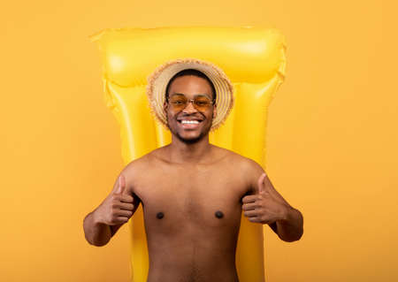 Top view of happy black man lying on inflatable lilo and showing thumbs up with both hands, yellow backgroundの写真素材