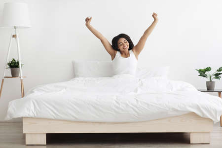 Happy african american lady sitting on bed