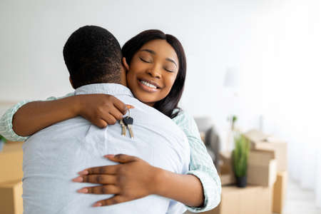 House ownership concept. Excited black woman holding house key and hugging her husband, free spaceの写真素材
