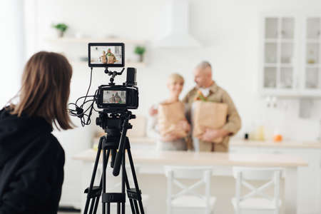 Happy senior caucasian woman and husband with eco packages after supermarket in kitchen interiorの写真素材