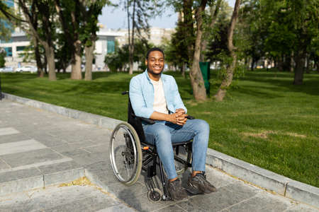 Accessible environment for disabled people concept. Happy black guy in wheelchair going down ramp on city streetの写真素材