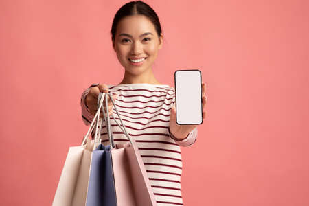 Online Shopping App. Asian woman holding bags showing smartphone with white screen