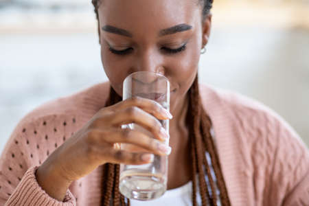 Refreshing Drink. Beautiful Young Black Lady Drinking Water From Glass At Homeの写真素材