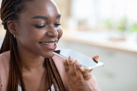 Smiling Young Black Female Using Virtual Voice Assistant Option On Smartphone