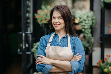 Smiling young attractive confident woman seller in apron crossed arms on chestの写真素材