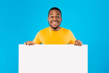 Black Guy Holding Empty White Paper Board Over Blue Backgroundの写真素材