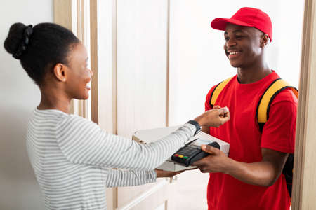 African Woman Paying Courier For Pizza With Smartwatch At Homeの写真素材
