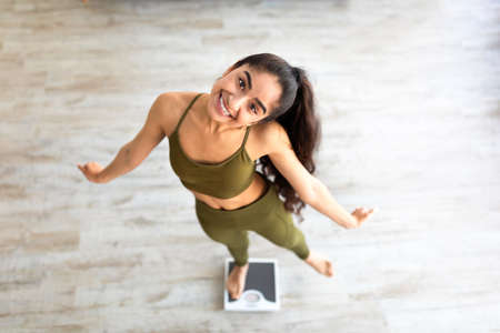 Above view of millennial Indian lady dancing on scales, choosing healthy lifestyle, happy with slimming resultの写真素材