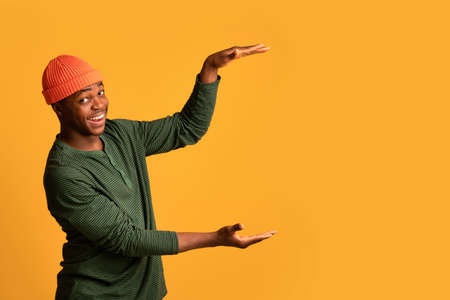 Positive Black Guy Holding Big Invisible Object In Hands Over Yellow Background