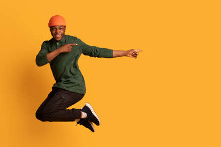 Look At This. Cherful african guy pointing aside while jumping in airの写真素材