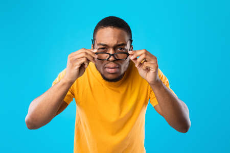 African American Man Squinting Eyes Looking Through Eyeglasses, Blue Backgroundの写真素材