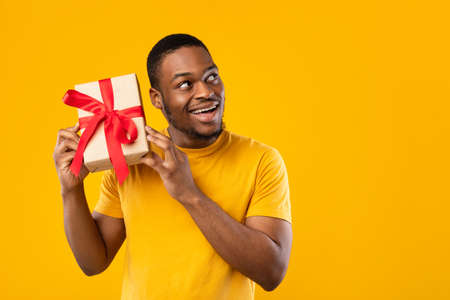 Funny African Guy Holding Gift Guessing Whats Inside, Yellow Background