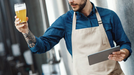 Handsome brewer examines beer from tanks in breweryの写真素材