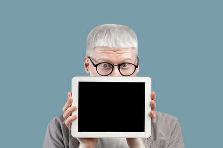 Young abino guy peeking out of tablet computer with blank screen over turquoise background, mockup for ad or designの写真素材