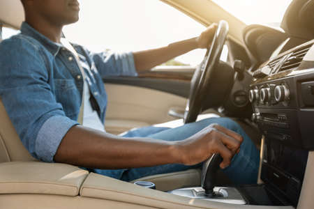 Unrecognizable black guy holding hand on gear, driving car
