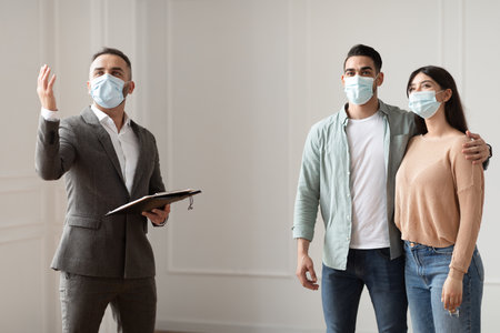 Estate Agent In Medical Mask Showing Buyers New Apartmentの写真素材
