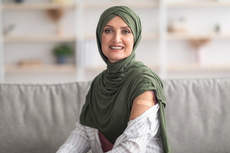 Happy Vaccinated Muslim Woman Showing Arm With Plaster Bandage Indoorの写真素材
