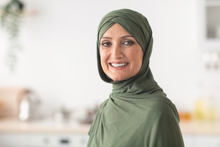 Portrait Of Happy Mature Muslim Lady Wearing Hijab In Kitchenの写真素材