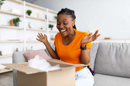 Satisfied female client opening cardboard box, excited over great delivery service, receiving online shop order at homeの写真素材