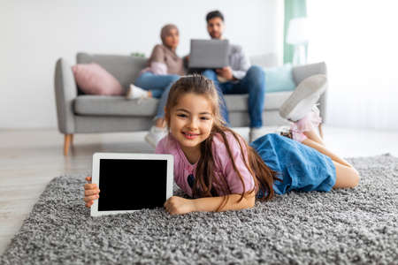 Little eastern girl showing digital tablet with empty screen, holding device with blank space for mockupの写真素材